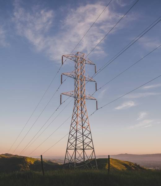 A vertical shot of an electric tower on a grassy field under a blue sky
